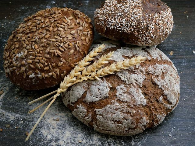 Fresh loaves of seeded bread with wheat stems on a dark table