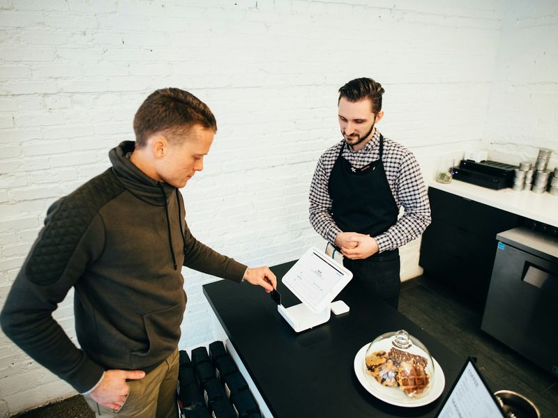 A café owner in an apron talking with a customer at the counter