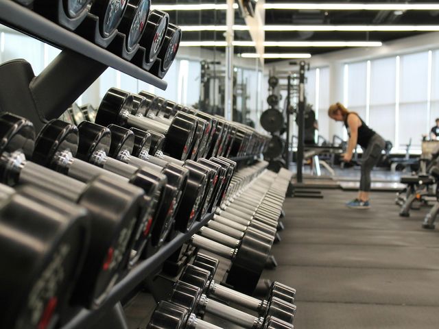 A bright gym with rows of dumbbells and a woman training