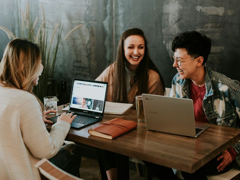 Three colleagues laughing together while one shows a website on her laptop