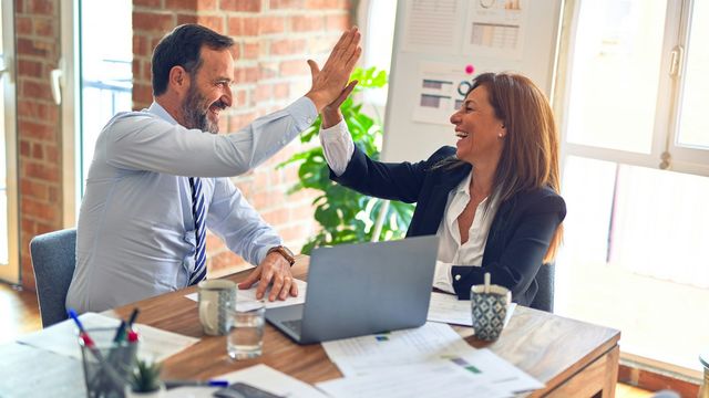 Two colleagues giving each other a high five across a meeting table