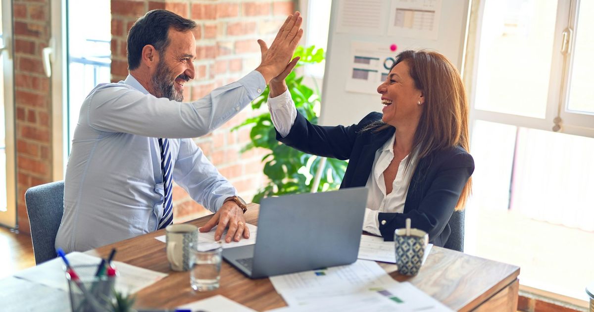 Two colleagues giving each other a high five across a meeting table