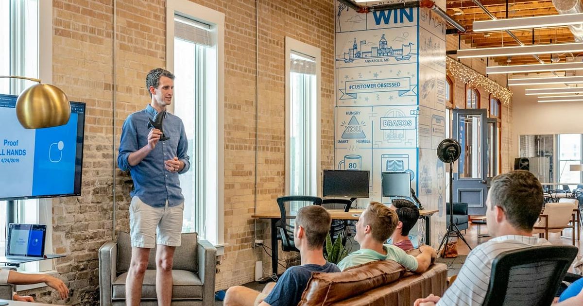 A man presenting to a small team in a bright brick-walled office
