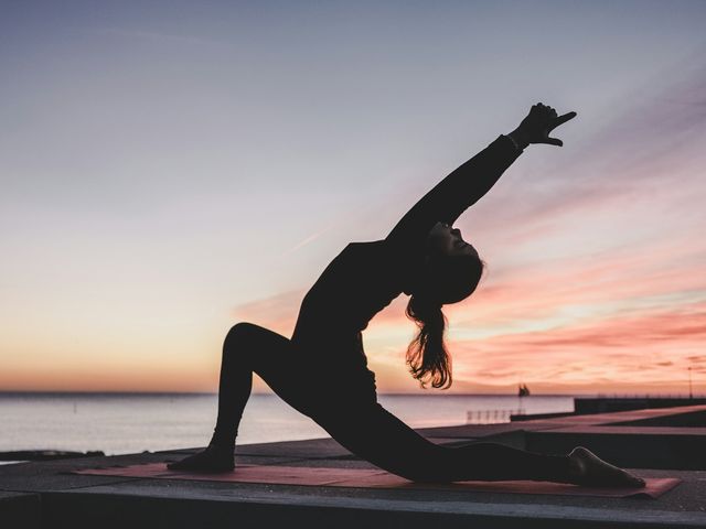 A woman in a yoga pose on a beach at sunset
